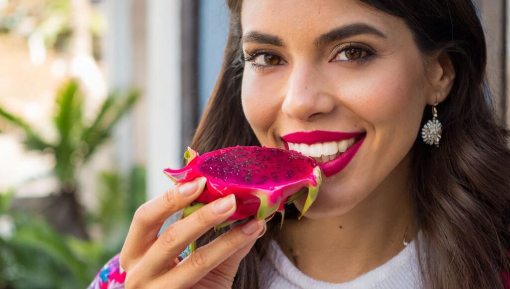 A young women with a slice of red dragon fruit